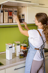 Laughing young female housewife posing during general cleaning, tidying up in cupboard kitchen