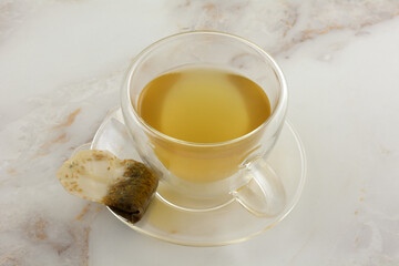 Lemon ginger tea in insulated glass teacup with used teabag on saucer