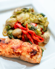 Coho Salmon grilled on white plate with vegetables in a shallow background