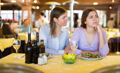 Caring woman calming her upset female friend while sitting together at table in cozy restaurant during dinner..