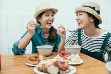Fototapeta premium Group of young female friends wearing straw hats enjoying taiwanese local meal in street food vendor. cheerful ladies smiling holding spoon eating tasty dishes indoors together. happy women tourists