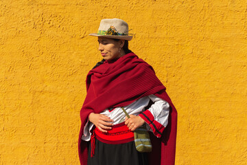 Hispanic peasant woman in traditional dress posing in front of a rustic yellow wall