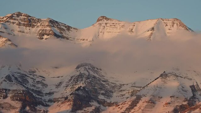 Timelapse of clouds moving across Timpanogos Mountain at sunset covered in snow during winter in Utah.