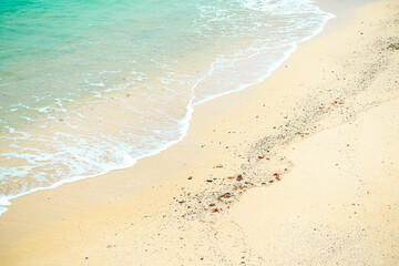 Clear water with small white waves hitting the light yellow sand