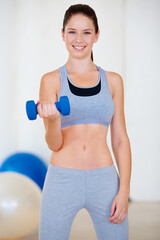 Shes happy when shes exercising. Portrait of an attractive young woman doing bicep curls with a dumbbell.