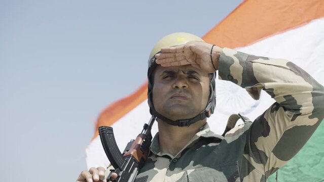 close up shot of soldier with gun hand looking around on hill top with flying indian flag in background - concpet of border protection force, serviceman on duty and security