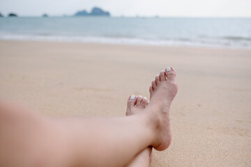 Closeup image of a female's legs and feet while sitting by the sea with blue sky background
