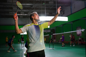 a healthy senior man is playing badminton in badminton sport stadium,concept of elderly people hobby,lifestyle,health,competition etc - obrazy, fototapety, plakaty