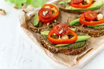 Dietary vegetarian sandwiches with cereal bread, vegetables and spicy sauce on a wooden plate on a white table. healthy eating. Side view, close-up, space for text.