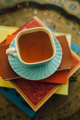 hot tea in teal square teacup on top of colorful stack of books
