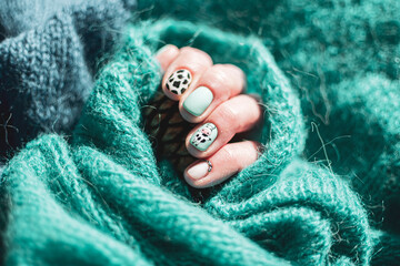 Cozy woven material and female hand closeup. Colorful threads, fresh neat manicure, funny nail design idea. Selective focus on the details, blurred background.