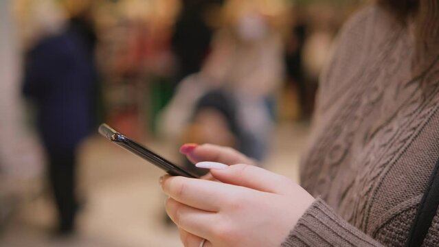 young woman holding a phone on the background of a supermarket. The girl is holding a smartphone in the mall. Business woman working on smartphone surfing the Internet.