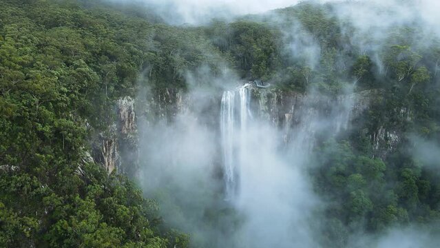 Unique view of a fog covered mountain revealing a majestic tropical waterfall lookout platform. Cinematic drone view
