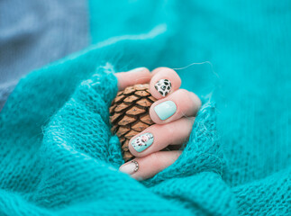 Delicate pastel colors on stylish fingernails. Female hand with funny creative manicure wrappet in knitted sweater. Selective focus on the details, blurred background.
