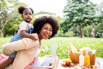 Portrait of beautiful mom and daughter relaxing with bright smiling and using laptop computer at the park. Spending free time doing family activities during the holidays