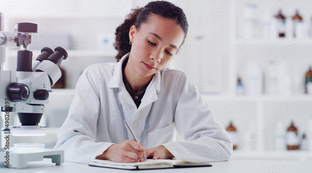 Wall mural investigating one matter after another. shot of a young scientist writing notes while working in a l