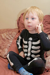 A child in a skeleton costume sits on the couch with an emotion on his face - 490263301