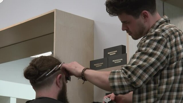Male barber uses trimmer, shapes hairline on bearded customer undercut