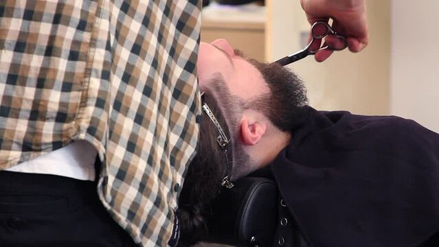 Close up of barber trimming customer's hipster beard with shears
