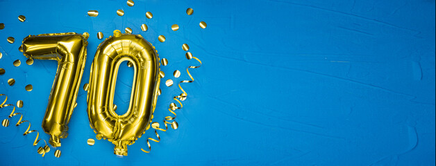 golden yellow foil balloon on blue concrete background number seventy. Birthday or anniversary card...