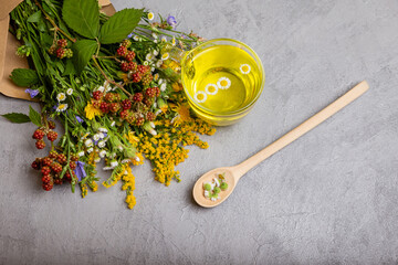 Various kinds of herbal tea. Cup of herbal tea with herbs on grey background. Cup of healthy herbal tea and camomile flowers in spoon. Summer healthy herbal tea in cup and bunches of healing herbs