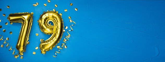 golden yellow foil balloon on blue concrete background number seventy nine. Birthday or anniversary card with 79 inscription. Anniversary celebration.