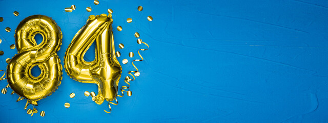 golden yellow foil balloon on blue concrete background number eighty four. Birthday or anniversary...