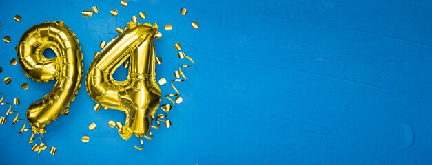 golden yellow foil balloon on blue concrete background number ninety four. Birthday or anniversary...