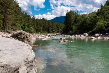 River Gail flowing through the Schuett in the natural park Dobratsch in Villach, Carinthia, Austria. Gailtaler and Villacher Alps. Riverbank is full of massive rocks. Swimming in crystal clear water