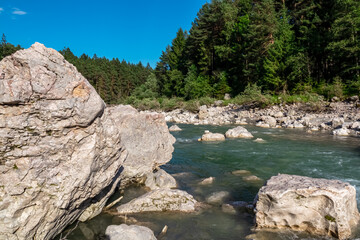 River Gail flowing through the Schuett in the natural park Dobratsch in Villach, Carinthia, Austria. Gailtaler and Villacher Alps. Riverbank is full of massive rocks. Swimming in crystal clear water