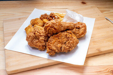 Fried chicken Crispy Chicken and Soft Chicken on white paper with nuggets and french fries on wooden table.