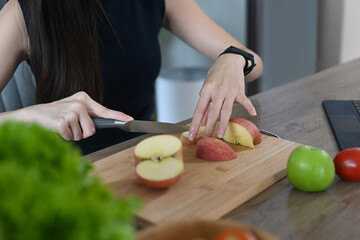 Young woman cutting fruits on a wooden board while making healthy breakfast in home kitchen.