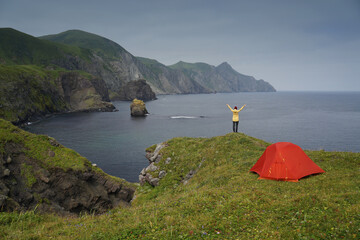 Traveler Standing and Hands Raising on the Cliff and Looking at the Pacific Ocean Coastline on Shikotan Island, Lesser Kuril Chain, Russia.