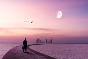 A lonely man is standing on a wooden pier and looking to the horizon with lilac sky and moon