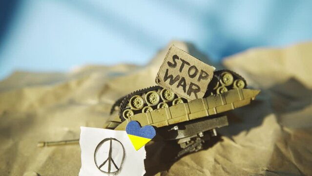 Overturned toy tank with peace symbol, Ukraine flag colored heart-shaped and stop war placard