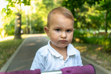 cute little boy with serious look looks at camera. sad, offended child. Child is naughty in park....
