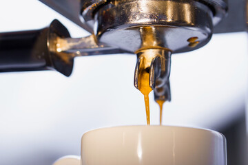 Fresh coffee pouring down from portafilter of espresso machine into white ceramic cup. Close up