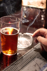 Indulging in bad habits. Cropped shot of a mans hand holding a cigarette and a glass of beer on the counter.