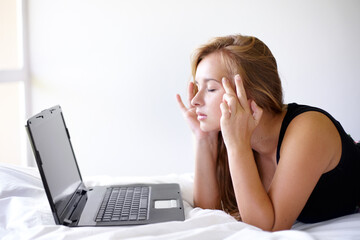 Getting some online advice for migraines. Shot of a beautiful young woman looking frustrated while using a laptop on her bed.