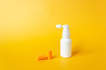 Plastic blank ear spray bottle with nozzle and orange earplugs isolated on yellow background. For...