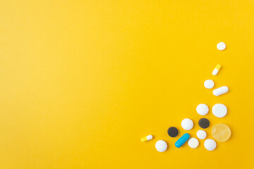 Pattern of multicolored pills and capsules in the lower right corner. Yellow background.Healthcare and wellbeing concept