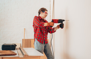 Laborer girl in protective glasses drills concrete wall with drill.