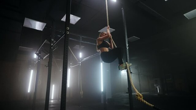 woman is climbing rope in fitness center, physical exercise developing endurance and power of arms