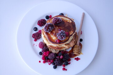 Pancakes with berries and honey on white table