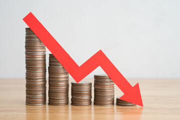Stack of coins bar chart and red graph trending downwards with white wall background on wooden...