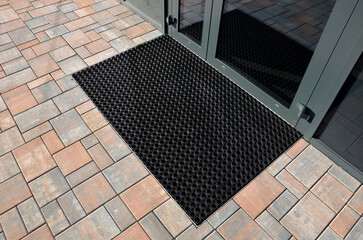 industrial mat cleaning zones at the entrance to the building. A black plastic-metal mat in the shape of an arch or half-circle lies on the limestone mosaic tiles - obrazy, fototapety, plakaty