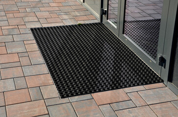 industrial mat cleaning zones at the entrance to the building. A black plastic-metal mat in the shape of an arch or half-circle lies on the limestone mosaic tiles - obrazy, fototapety, plakaty