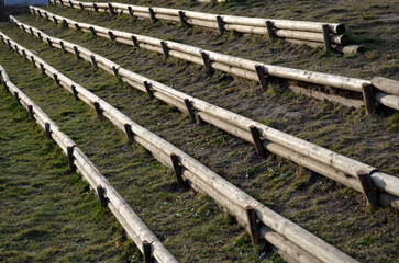 the grandstand on the village forball field or in the school yard. the stilts form rows of palisades for sitting. the slope is stabilized by rows of stakes in rows above each other on the hill - obrazy, fototapety, plakaty