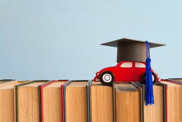 Red wooden car toy with graducate cap on textbook blue wall background copy space - Back to school, education and scholarship abroad concept. Education is future planning. - obrazy, fototapety, plakaty