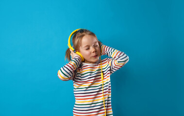 portrait of a cute charming girl listening to her favorite song with yellow headphones on a blue background